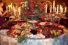 a table topped with lots of food next to tall candles and plates filled with fruit