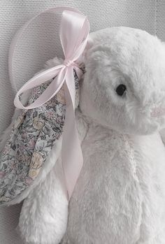 a white teddy bear with a pink ribbon around its neck sitting next to a pillow