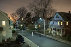 an empty street at night with some houses in the background and one car parked on the side