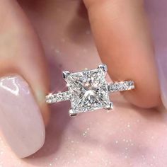 a woman's hand with a diamond ring on top of her finger and the other hand holding an engagement ring