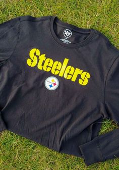 a black shirt with the word pittsburgh on it laying in the grass next to a pair of scissors