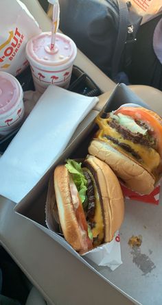 two cheeseburgers with fries and drinks in the back seat of a car on a road trip