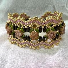 a close up of a bracelet on a white cloth with gold and pink beading