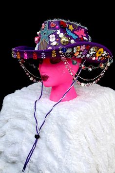 All eyes will be on you in this fabulous purple cowgirl hat covered to the brim with rainbow galore. From the front hang colorful gummy bears and from the sides hang three colorful beaded chains. The hat is covered with stars, hearts, flowers, rhinestones, butterflies, pearls, disco balls, mini animals and treats, and silver tinsel. It has a purple and lace neck tie. Playful Purple Adjustable Hat, Purple Wide Brim Adjustable Costume Hat, Purple Adjustable Wide Brim Costume Hat, Adjustable Wide Brim Purple Mini Hat, Trendy Brimmed Mini Hats For Festival, Multicolor Beaded Party Hats, Adjustable Western Purple Hat, Trendy Adjustable Mini Hats For Festivals, Funky Adjustable Party Hats