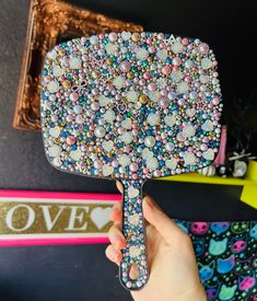 a person holding up a colorful hair brush with lots of beads on it's face