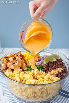 someone pouring dressing into a bowl filled with pasta and veggies, including chicken