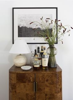 a wooden cabinet with bottles and vases on it next to a framed photograph in the corner