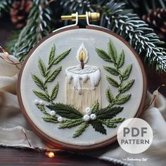 a white cake with a lit candle surrounded by green leaves and pine cones on a wooden table