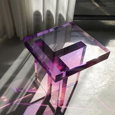 a purple glass table sitting on top of a floor next to a window with white curtains