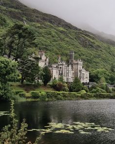 an old castle sits on the side of a hill next to a body of water