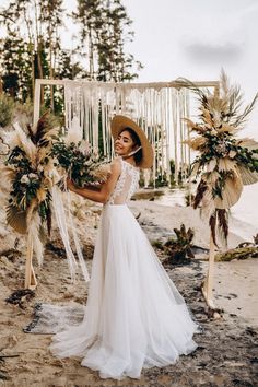 a woman in a white dress and straw hat standing on the beach next to some flowers