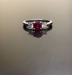 DeKara Designs Collection Classic/Modern Three Stone Diamond Past Present and Future Engagement Ring. Metal- 90% Platinum, 10% Iridium Stones- 1 Round Natural Pigeon Blood Ruby 0.71 Carats, 2 Round Diamonds, G color VS1 clarity, .44 carats. Art Deco Inspired Beautiful Pigeon Blood Red Ruby Three Stone Diamond Engagement Ring Made in Platinum. There is a vibrant and fiery round ruby that is professionally set in between four prongs. There is one round fiery diamond on each side of the the ruby th Luxury Gia Certified White Gold Ruby Ring, Luxury Ruby Ring With Round Cut And Prong Setting, Luxury Ruby Ring With Prong Setting, Luxury Round Cut Ruby Ring With Prong Setting, Gia Certified Fine Jewelry Ruby Ring In Platinum, Gia Certified Platinum Ruby Ring In Fine Jewelry, Gia Certified Platinum Ruby Ring, Gia Certified Round Cut Ruby Ring Fine Jewelry, Diamond White Ruby Ring With Center Stone