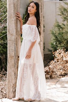 a woman standing next to a tree wearing a white dress