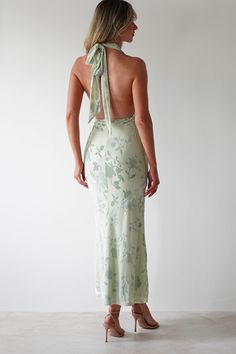 the back of a woman wearing a green dress with floral print and halter neck