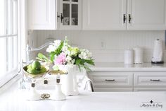 a white kitchen with flowers and fruit on the counter