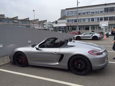 a silver porsche sports car parked in a parking lot next to a building with people standing around it