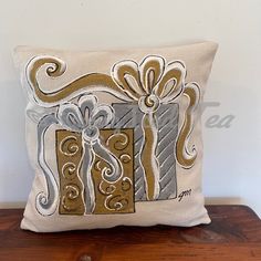 a decorative pillow with a gift box on the front and bow at the back, sitting on a wooden table