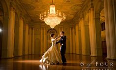 a bride and groom dancing in an ornate ballroom with chandelier above the dance floor