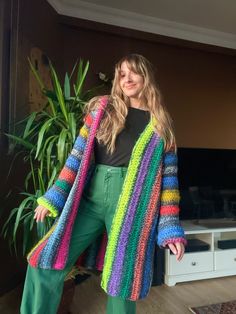 a woman standing in front of a plant wearing a colorful cardigan