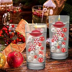 two glass candles are sitting on a table with christmas decorations and ornaments around the candle