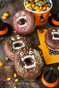 decorated doughnuts with sprinkles and candy eyes on wooden table next to halloween decorations