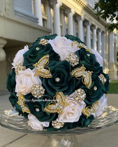 a bridal bouquet with green and white flowers on a glass platter in front of a building