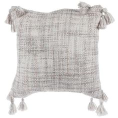 a gray and white pillow with tassels on the front, sitting on a white background