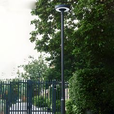 a lamp post in front of a fence and some trees with green leaves on it