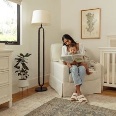 a woman sitting in a chair reading a book to her baby