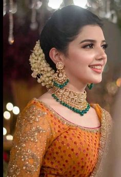 a woman in an orange and gold lehenga with green jewelry on her neck