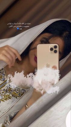 a woman taking a selfie with her cell phone in the mirror while wearing a white shawl