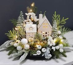 a christmas centerpiece with white and green decorations on top of a table next to a lit up house