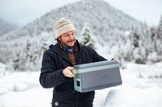 a man standing in the snow holding a box with an electronic device on top of it