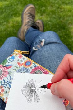 a person holding a pen and drawing on paper with a flower design in front of them