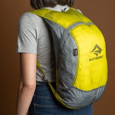 a woman wearing a yellow and grey backpack with the back pocket open to show the logo