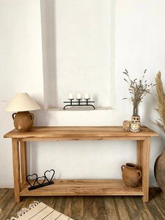 a wooden table sitting on top of a hard wood floor next to a vase and lamp