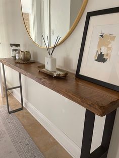 a long wooden table with a mirror and vase on it next to a framed photograph