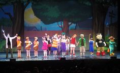 a group of people standing on top of a stage in front of a tree filled forest