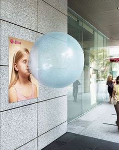 a woman walking past a building with a giant balloon attached to the side of it