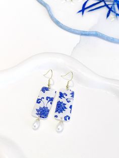 a pair of blue and white earrings sitting on top of a table next to flowers