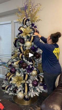 a woman decorating a christmas tree with purple and gold decorations on it's top