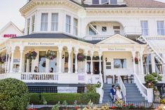 two people standing in front of a large white building with flowers on the porch and steps leading up to it