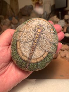 a hand holding a rock with a dragonfly painted on it