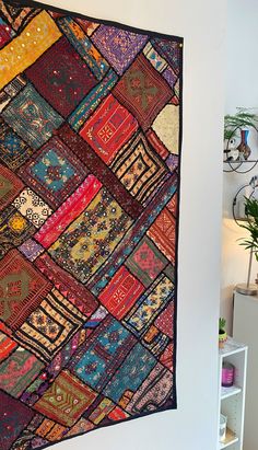 a multicolored patchwork quilt hanging on the wall next to a white shelf