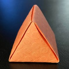 an orange piece of paper sitting on top of a black table next to a blue background