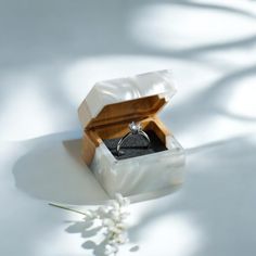 an open ring box sitting on top of a white surface with a flower in it