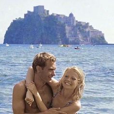 a man holding a woman in his arms while standing on the water near an island