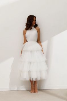 a woman standing in front of a white wall wearing a dress with tiered layers