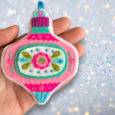 a hand holding a pink ornament with green and blue trimmings on it