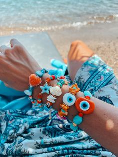 a close up of a person laying on the beach wearing bracelets with seashells